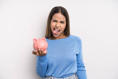 Neşeli ve asi tavırlı, şaka yapan ve dilini dışarı çıkaran İspanyol asıllı güzel bir kadın. Domuz kumbarası konsepti