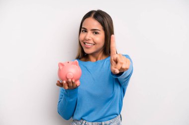 Hispanik güzel kadın gururla gülümsüyor ve kendinden emin bir numara oluyor. Domuz kumbarası konsepti