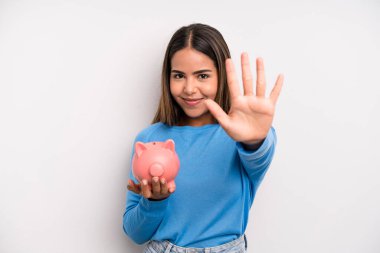 İspanyol güzel kadın gülümsüyor ve arkadaş canlısı görünüyor, beş numarayı gösteriyor. Domuz kumbarası konsepti