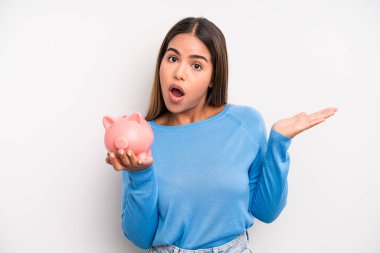 İspanyol güzel kadın şaşırmış ve şok olmuş görünüyor. Çenesi düşmüş ve elinde bir nesne var. Domuz kumbarası konsepti