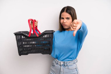 hispanic pretty woman feeling cross,showing thumbs down. empty supermarket basket concept