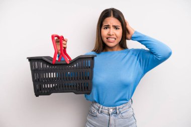 hispanic pretty woman feeling stressed, anxious or scared, with hands on head. empty supermarket basket concept