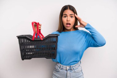 hispanic pretty woman looking happy, astonished and surprised. empty supermarket basket concept