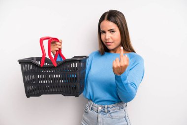 hispanic pretty woman feeling angry, annoyed, rebellious and aggressive. empty supermarket basket concept