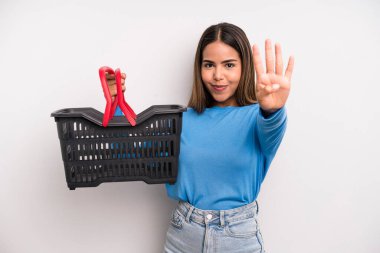 hispanic pretty woman smiling and looking friendly, showing number four. empty supermarket basket concept