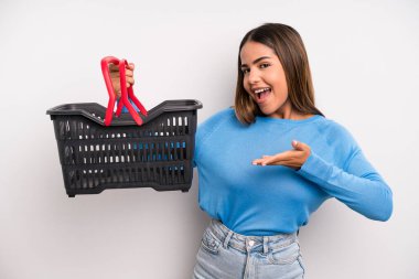 hispanic pretty woman smiling cheerfully, feeling happy and showing a concept. empty supermarket basket concept