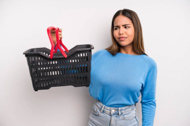 hispanic pretty woman feeling sad, upset or angry and looking to the side. empty supermarket basket concept