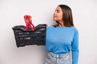 hispanic pretty woman on profile view thinking, imagining or daydreaming. empty supermarket basket concept