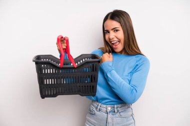 hispanic pretty woman feeling happy and facing a challenge or celebrating. empty supermarket basket concept