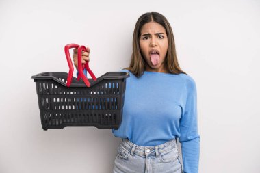 hispanic pretty woman feeling disgusted and irritated and tongue out. empty supermarket basket concept