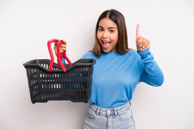 hispanic pretty woman feeling like a happy and excited genius after realizing an idea. empty supermarket basket concept
