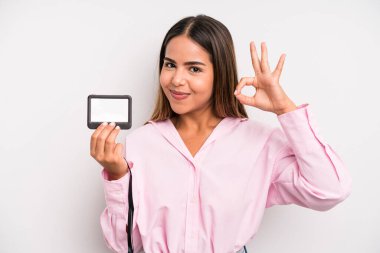 hispanic pretty woman feeling happy, showing approval with okay gesture. pass id card concept