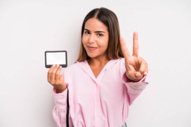 hispanic pretty woman smiling and looking happy, gesturing victory or peace. pass id card concept