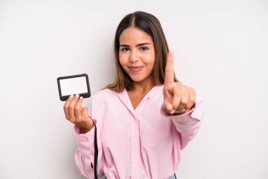 hispanic pretty woman smiling and looking friendly, showing number one. pass id card concept