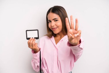 hispanic pretty woman smiling and looking friendly, showing number three. pass id card concept
