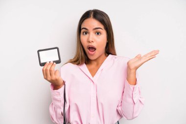 hispanic pretty woman looking surprised and shocked, with jaw dropped holding an object. pass id card concept