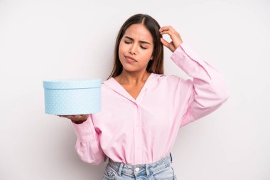 hispanic pretty woman feeling puzzled and confused, scratching head. gift box concept