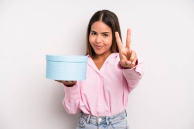 hispanic pretty woman smiling and looking happy, gesturing victory or peace. gift box concept