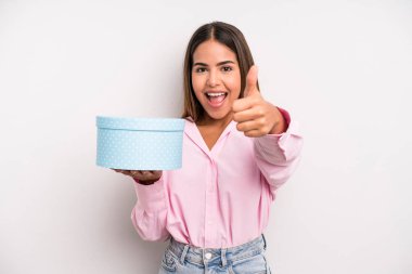 hispanic pretty woman feeling proud,smiling positively with thumbs up. gift box concept