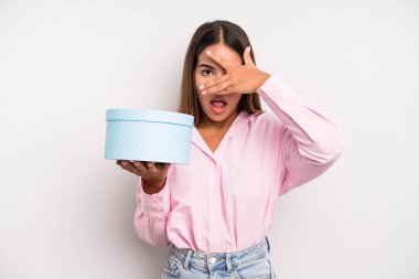 hispanic pretty woman looking shocked, scared or terrified, covering face with hand. gift box concept