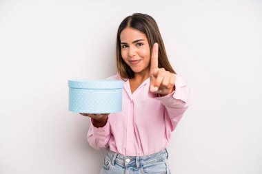 hispanic pretty woman smiling and looking friendly, showing number one. gift box concept