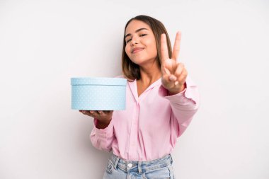 hispanic pretty woman smiling and looking friendly, showing number two. gift box concept