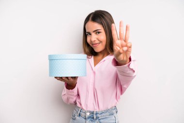 hispanic pretty woman smiling and looking friendly, showing number three. gift box concept
