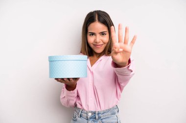 hispanic pretty woman smiling and looking friendly, showing number four. gift box concept
