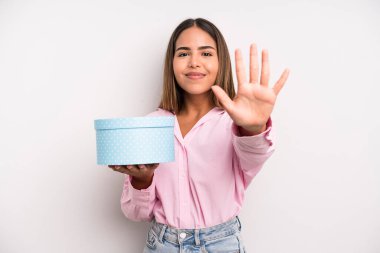 hispanic pretty woman smiling and looking friendly, showing number five. gift box concept