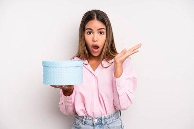 hispanic pretty woman looking surprised and shocked, with jaw dropped holding an object. gift box concept