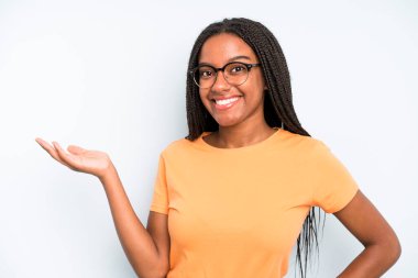 black young adult woman smiling, feeling confident, successful and happy, showing concept or idea on copy space on the side