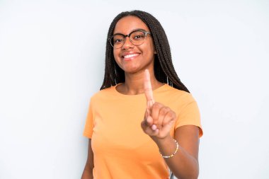 black young adult woman smiling proudly and confidently making number one pose triumphantly, feeling like a leader