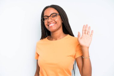 black young adult woman smiling happily and cheerfully, waving hand, welcoming and greeting you, or saying goodbye