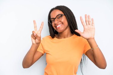 black young adult woman smiling and looking friendly, showing number seven or seventh with hand forward, counting down