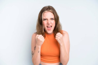 caucasian pretty woman shouting aggressively with annoyed, frustrated, angry look and tight fists, feeling furious