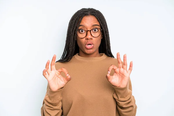 stock image black young adult woman feeling shocked, amazed and surprised, showing approval making okay sign with both hands