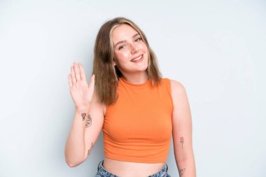 caucasian pretty woman smiling happily and cheerfully, waving hand, welcoming and greeting you, or saying goodbye