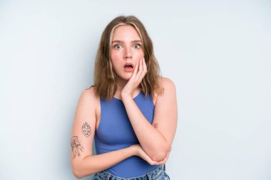 caucasian pretty woman open-mouthed in shock and disbelief, with hand on cheek and arm crossed, feeling stupefied and amazed