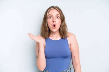 caucasian pretty woman looking surprised and shocked, with jaw dropped holding an object with an open hand on the side