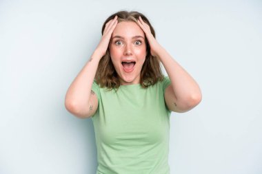 caucasian pretty woman raising hands to head, open-mouthed, feeling extremely lucky, surprised, excited and happy