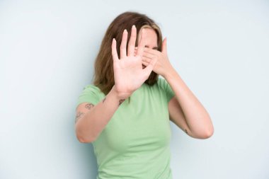 caucasian pretty woman covering face with hand and putting other hand up front to stop camera, refusing photos or pictures