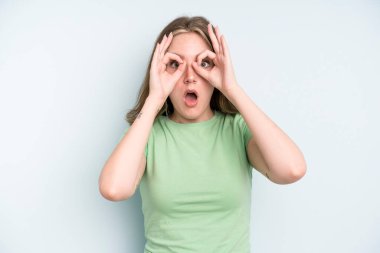 caucasian pretty woman feeling shocked, amazed and surprised, holding glasses with astonished, disbelieving look