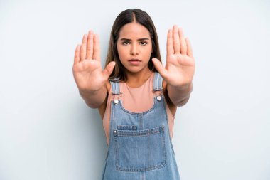 hispanic latin pretty woman looking serious, unhappy, angry and displeased forbidding entry or saying stop with both open palms