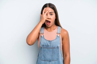hispanic latin pretty woman looking shocked, scared or terrified, covering face with hand and peeking between fingers