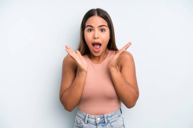 hispanic latin pretty woman looking happy and excited, shocked with an unexpected surprise with both hands open next to face