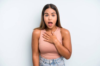 hispanic latin pretty woman feeling shocked and surprised, smiling, taking hand to heart, happy to be the one or showing gratitude