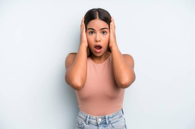 hispanic latin pretty woman looking unpleasantly shocked, scared or worried, mouth wide open and covering both ears with hands