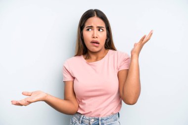 hispanic latin pretty woman shrugging with a dumb, crazy, confused, puzzled expression, feeling annoyed and clueless