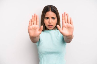 hispanic latin pretty woman looking serious, unhappy, angry and displeased forbidding entry or saying stop with both open palms