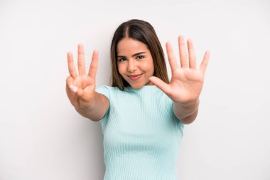 hispanic latin pretty woman smiling and looking friendly, showing number eight or eighth with hand forward, counting down